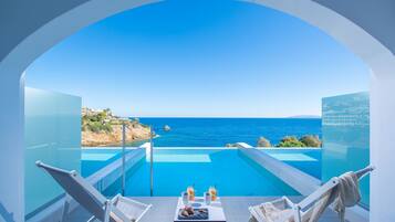 A balcony with a clear view of the sea, a table with drinks, and two lounge chairs.