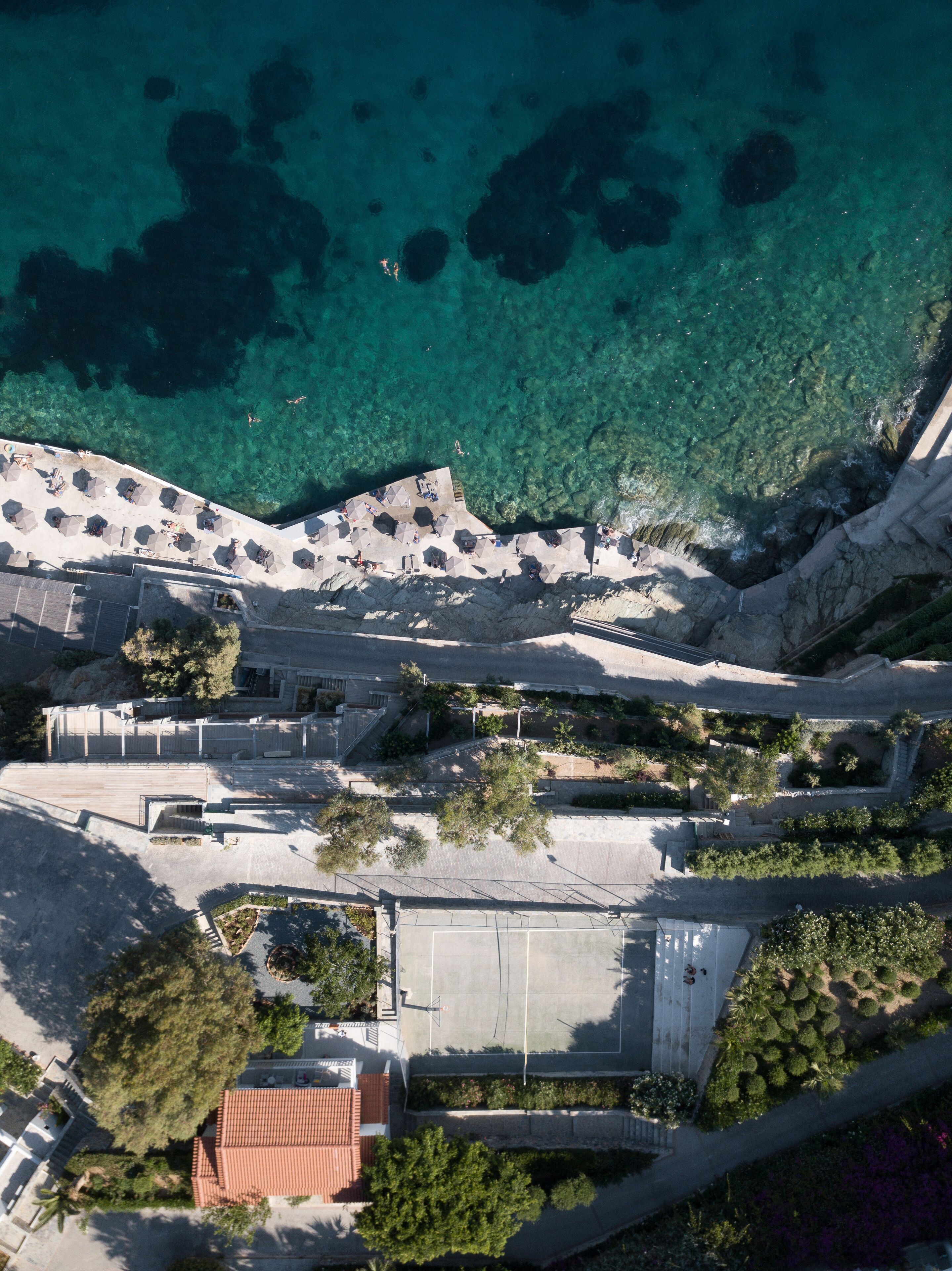 Vue aérienne d’une zone côtière avec des eaux cristallines, une promenade dallée et un parking.