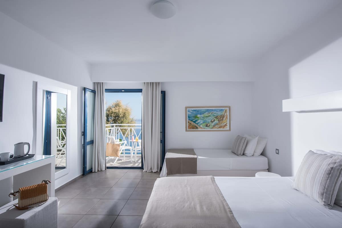 A modern hotel room with a bed, a sofa, a glass table, and a balcony with a view.