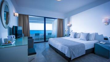 A modern hotel room with a bed, a desk, a chair, and a view of the sea.