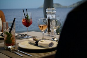 A table set with wine glasses, a water glass, and a plate with a napkin, overlooking a body of water. - Peninsula Resort & Spa - All Inclusive (Malevizi)