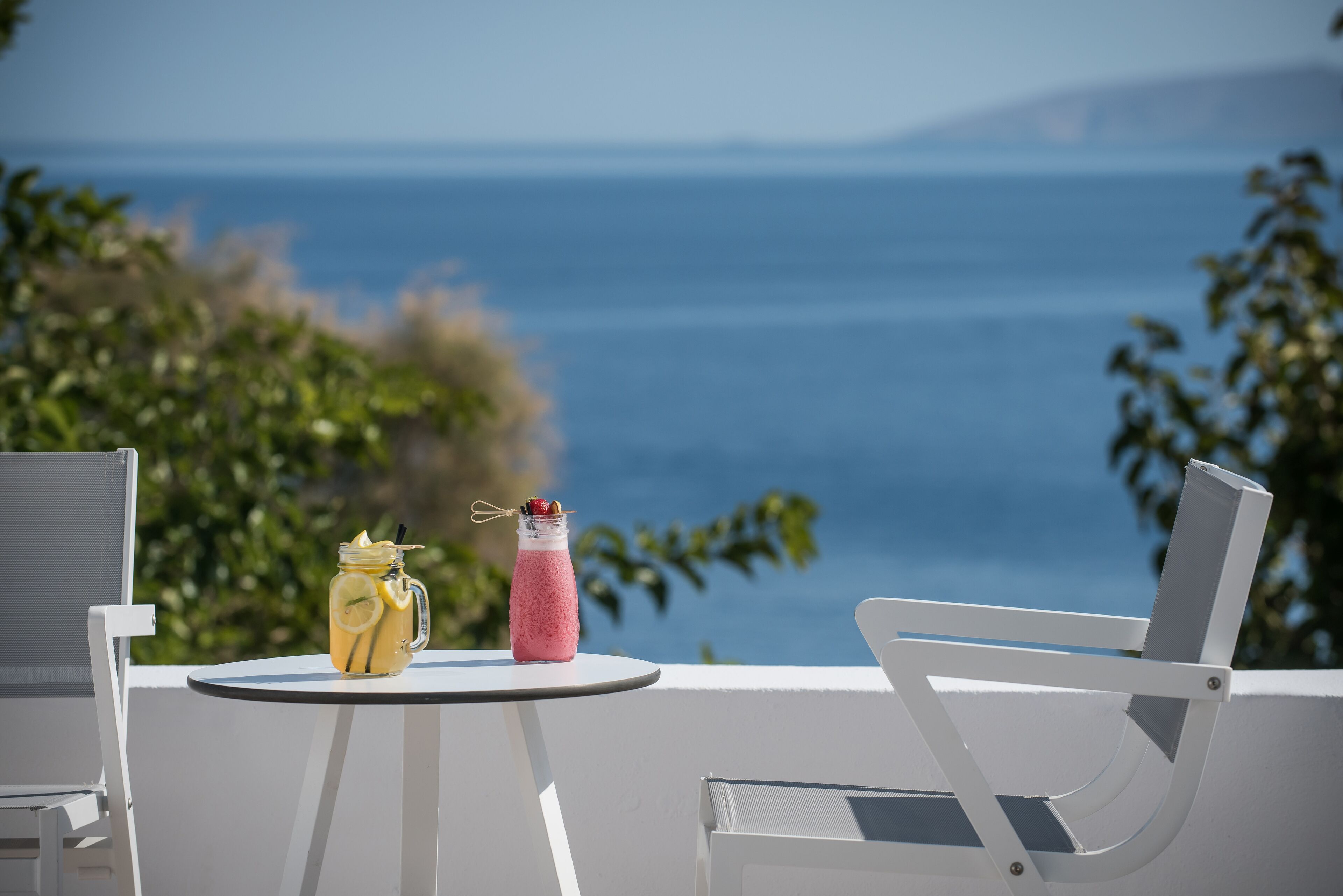 A table with a drink and a bottle, overlooking a scenic view of the sea.