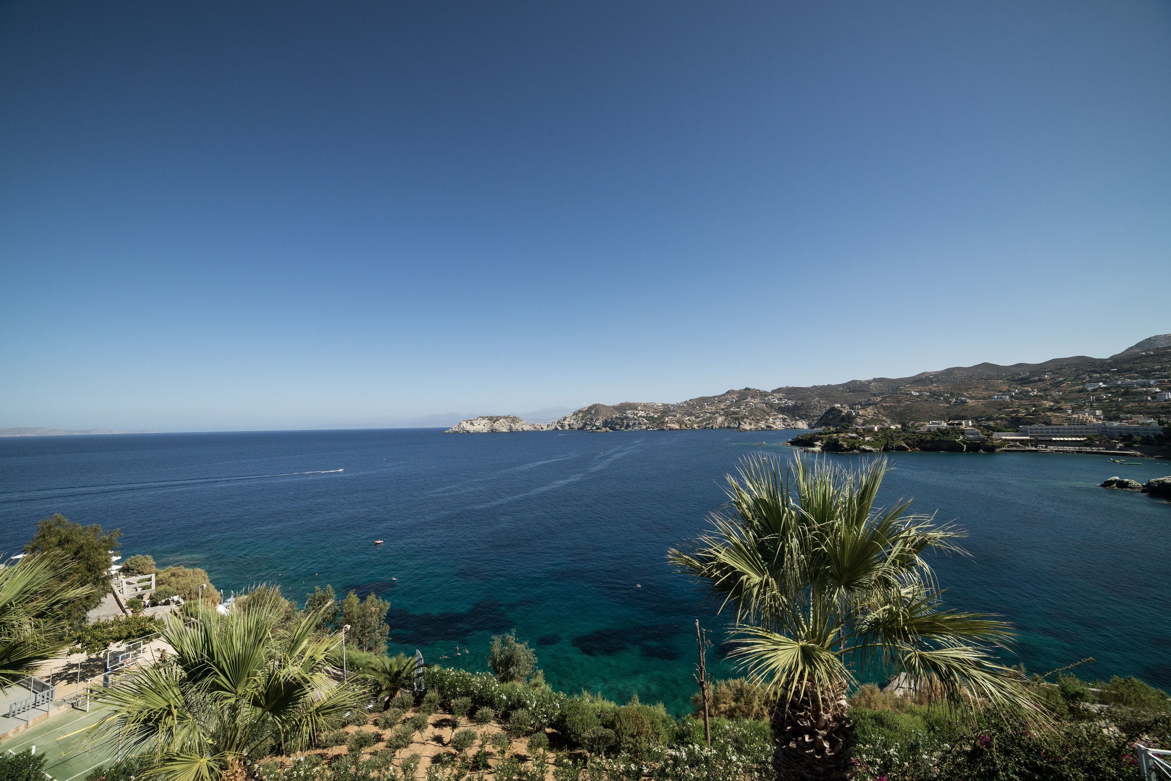 A coastal landscape with clear blue sea, rocky outcrops, and lush greenery.