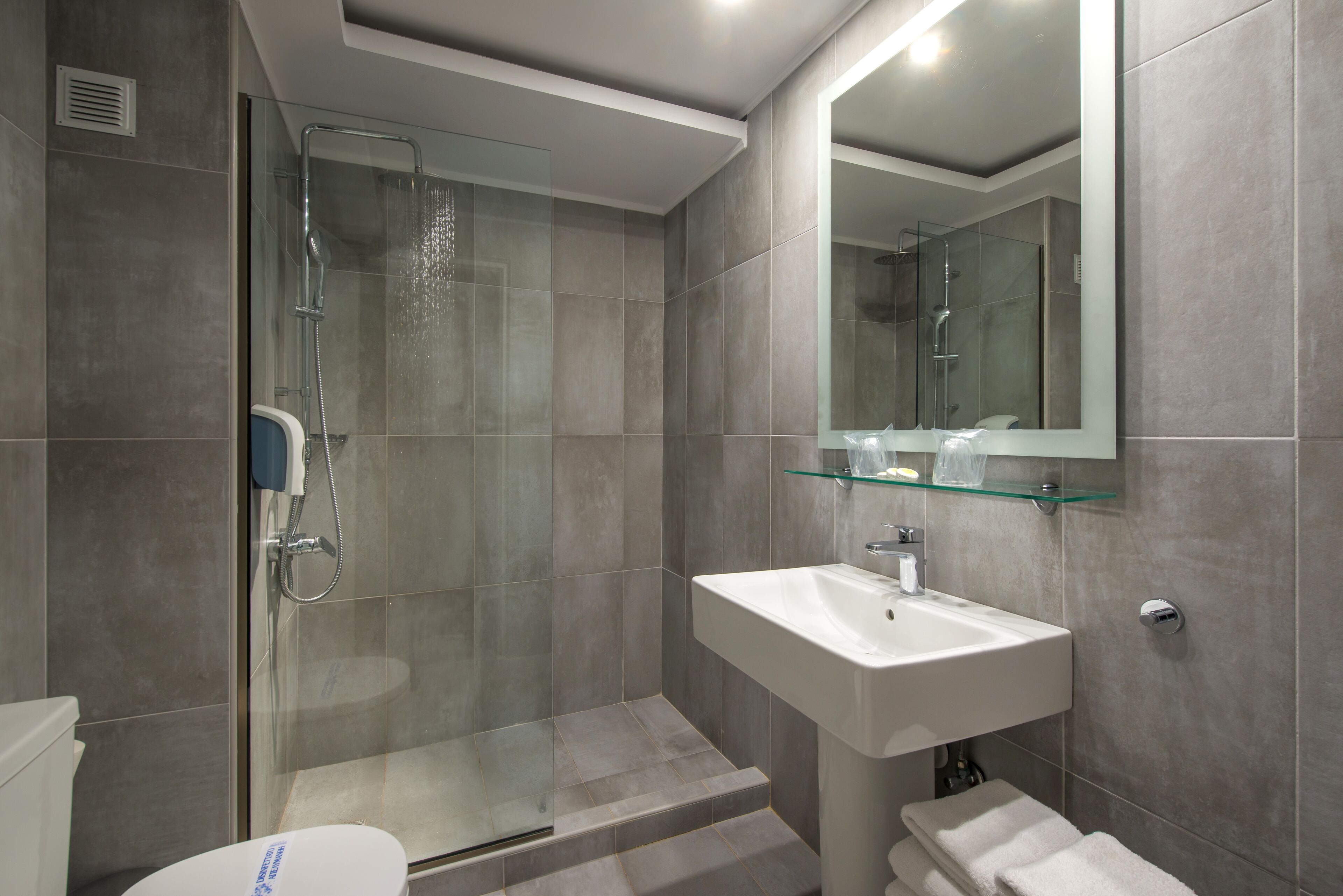 A modern bathroom with a glass-enclosed shower, a white sink, and a glass shelf above it.