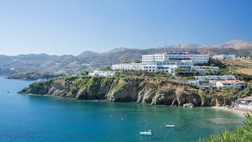 A coastal hotel with multiple white buildings, a rocky cliff, and clear blue sea.