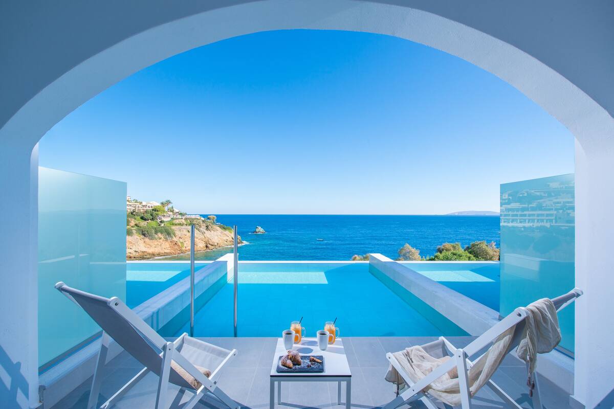 A balcony with a clear view of the sea, a pool, and two lounge chairs.