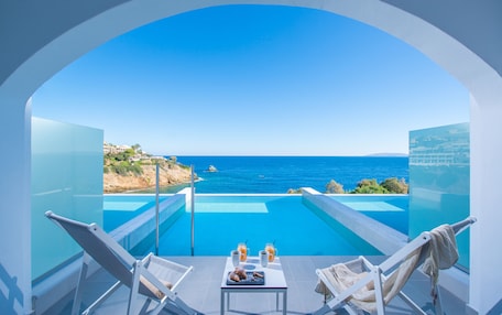 A balcony with a clear view of the sea, a pool, and two lounge chairs.