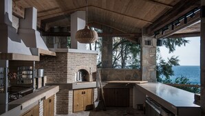 A kitchen with a stone wall, wooden beams, and a view of the sea. - Peninsula Resort & Spa - All Inclusive (Malevizi)