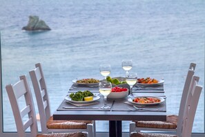 Una mesa de comedor con platos de comida y copas de vino blanco, frente a una vista al mar.