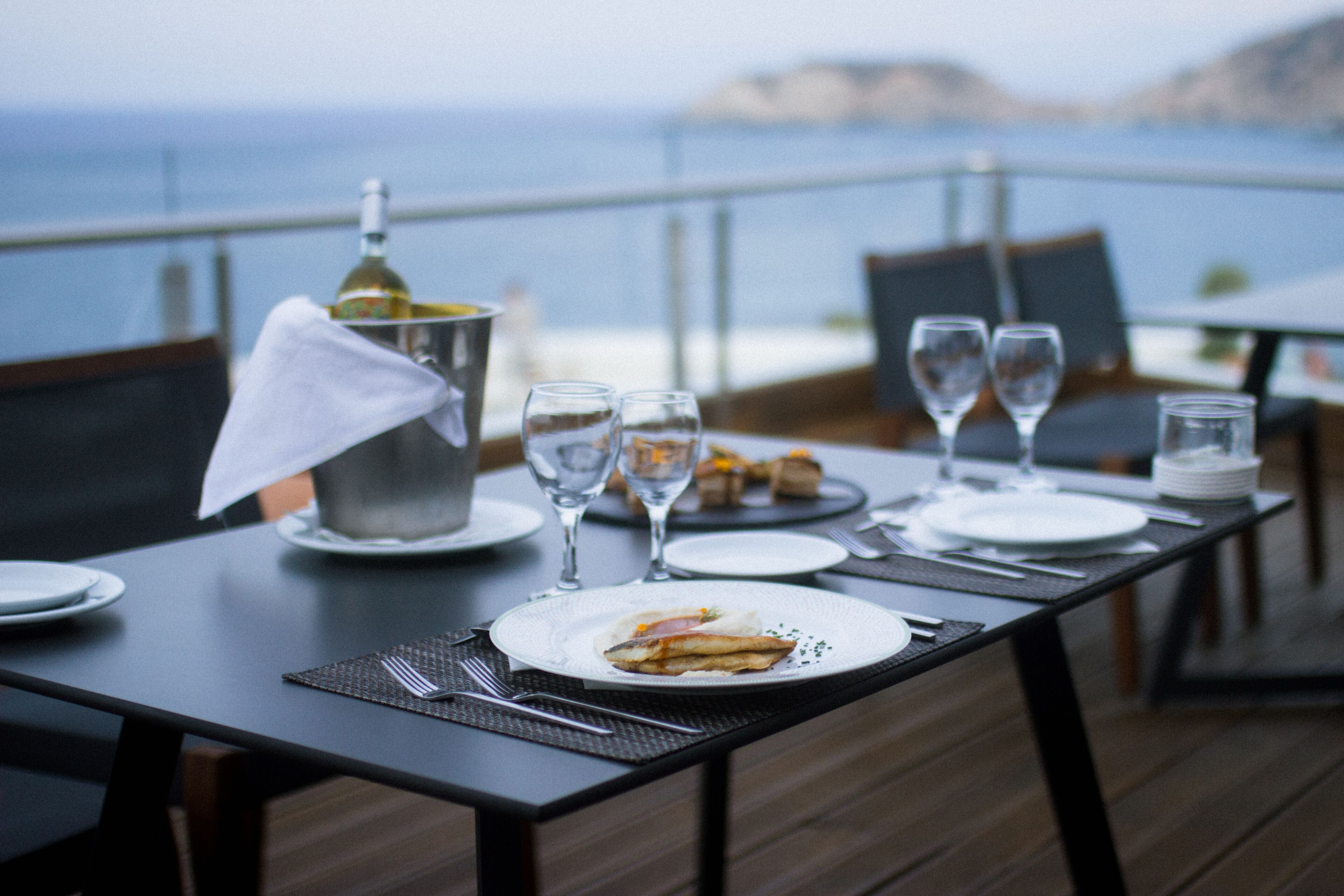 Mesa de comedor dispuesta con platos, vasos y una botella, con vistas a un paisaje pintoresco.