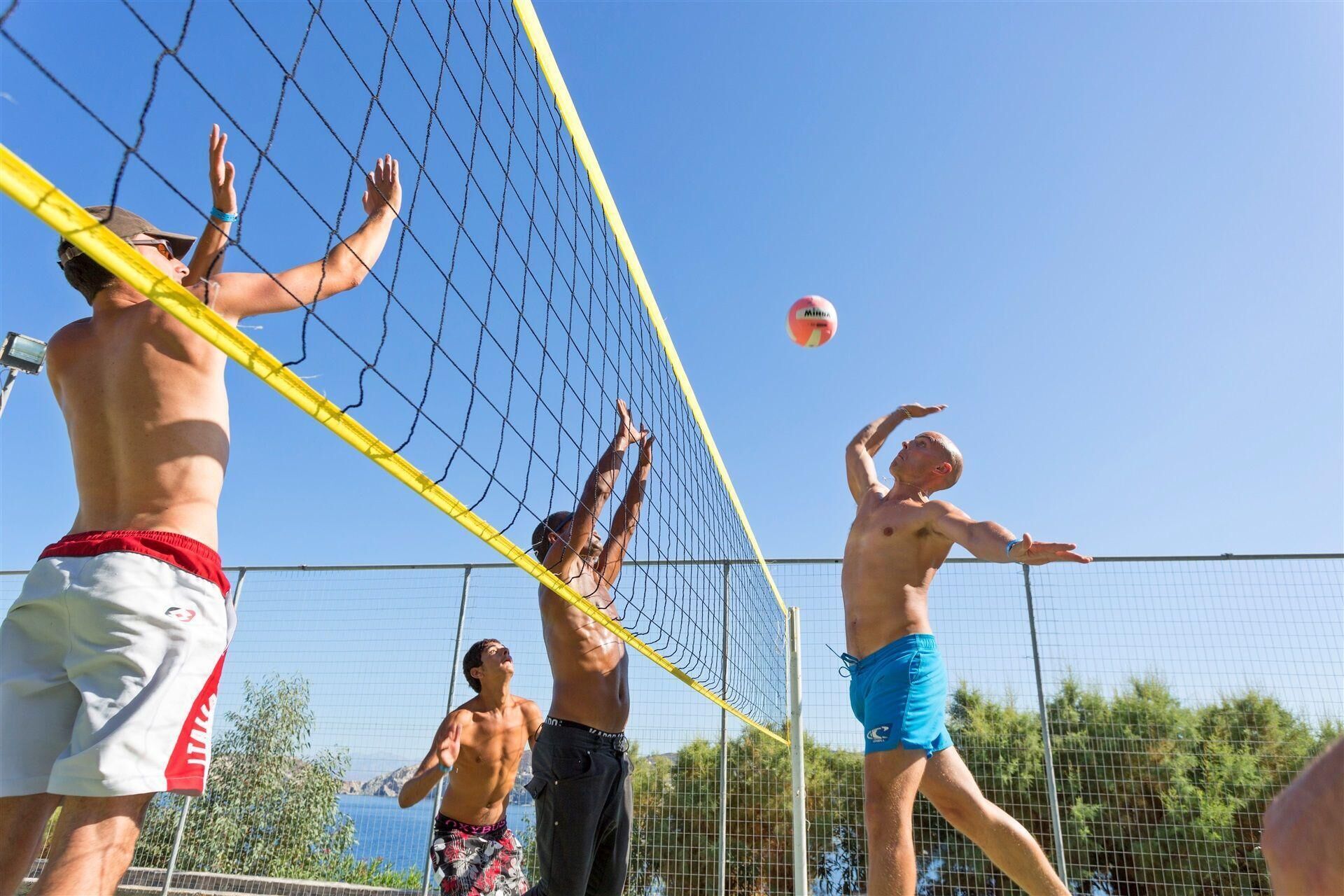 En gruppe mennesker spiller strandvolleyball i solskin.