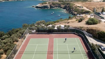 Un court de tennis où s’affrontent deux joueurs, le tout étant situé dans un cadre pittoresque en bord de mer.
