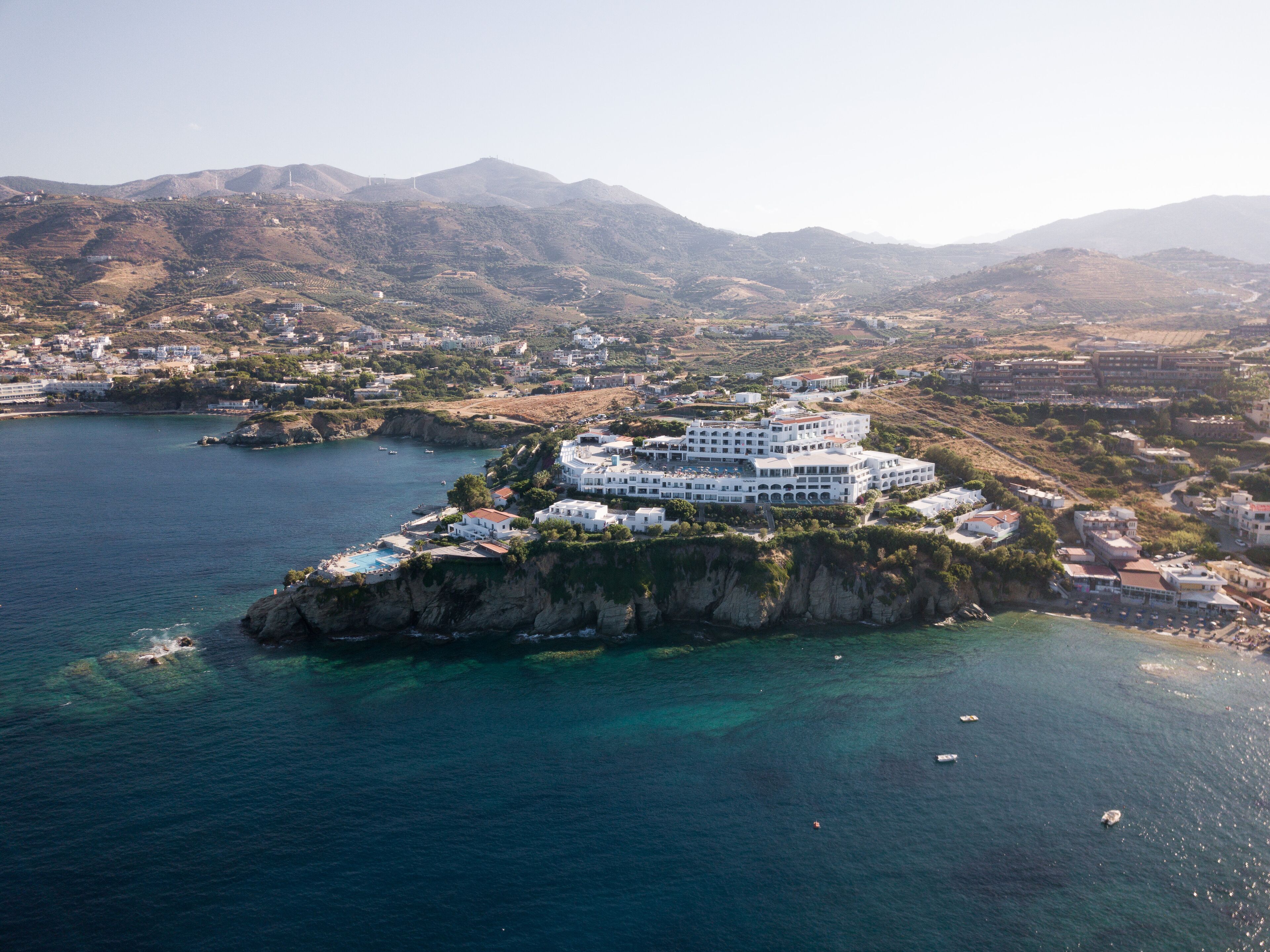 A coastal hotel with multiple white buildings, a swimming pool, and a view of the surrounding landscape.