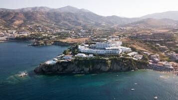 A coastal hotel with multiple white buildings, a swimming pool, and a view of the surrounding landscape.