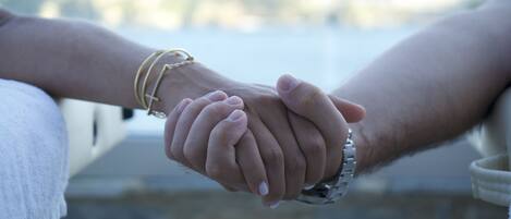 A close-up of two hands holding each other, with a blurred background suggesting a waterfront setting.