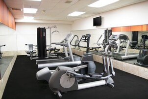 A gym with various exercise machines, a large mirror, and a flat-screen TV on the wall.