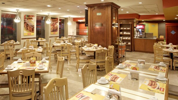 A restaurant with multiple tables and chairs, a counter with a beverage dispenser, and a menu board. - iStay Hotel Monterrey Histórico (Monterrey)