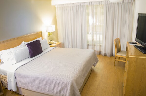 A hotel room with a bed, a desk, a chair, a television, and a window with curtains. - iStay Hotel Monterrey Histórico (Monterrey)