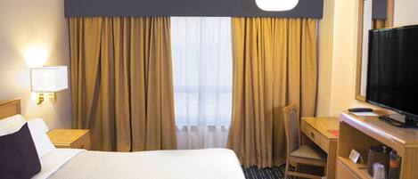 A hotel room with a bed, a desk, a chair, a television, and curtains.