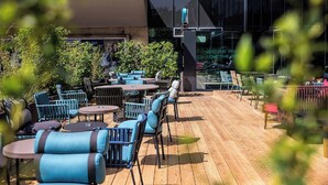 An outdoor patio area with round tables and chairs, surrounded by greenery. - Motel One Wien-Westbahnhof (Vienna)