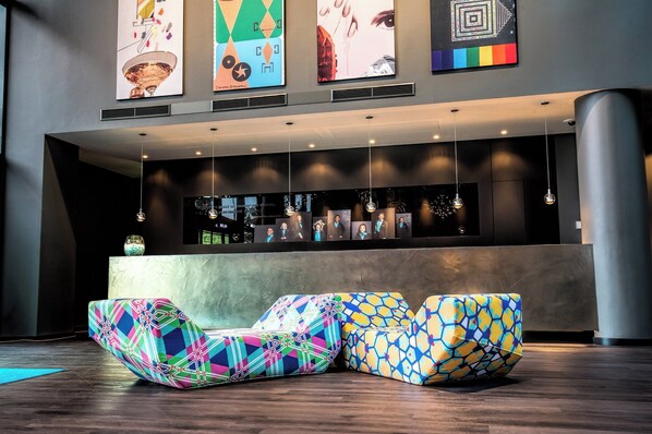 Un vestíbulo moderno con asientos de diseño geométrico y colores vibrantes, un mostrador de recepción y obras de arte en las paredes.