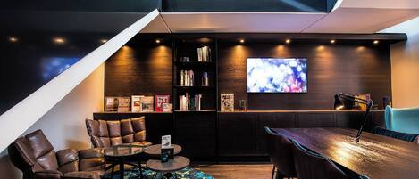 A modern interior with a sofa, a small round table, a bookshelf, and a flat-screen TV.