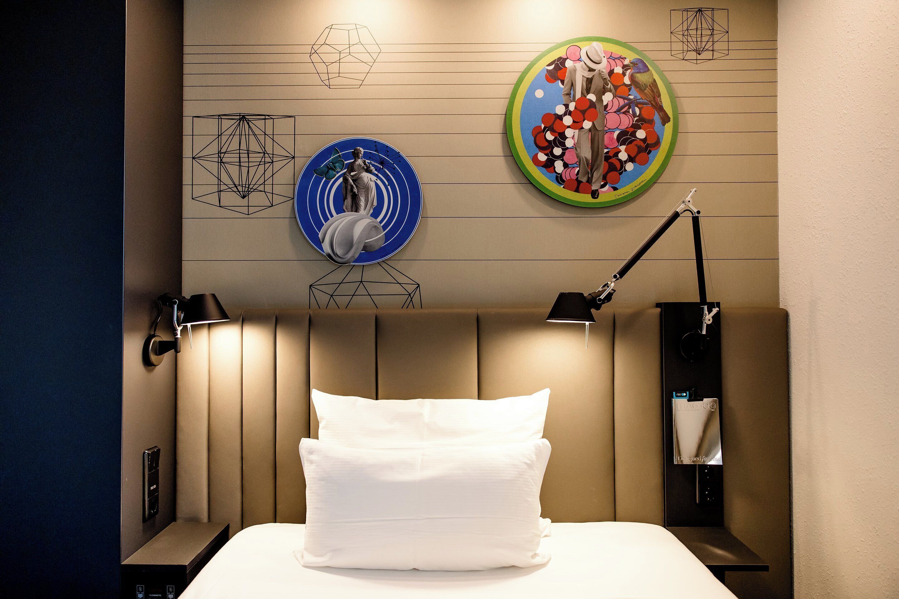 A hotel room with a bed, a nightstand, a lamp, and wall art.