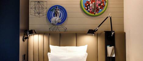 A hotel room with a bed, a nightstand, a lamp, and wall art.