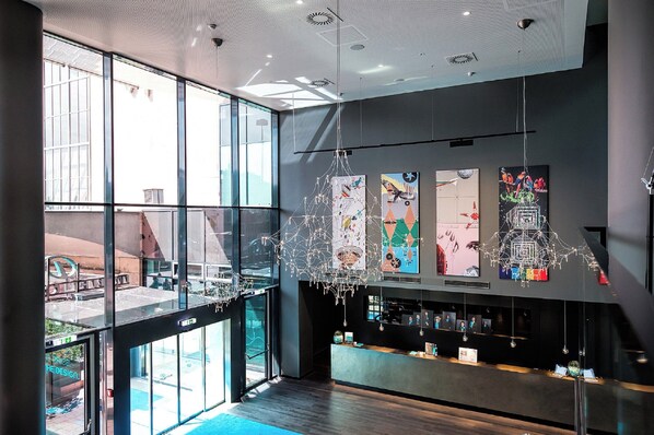 A modern interior with large windows, a suspended light fixture, and artwork on the walls. - Motel One Wien-Westbahnhof (Vienna)