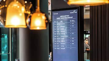 Ein modernes Interieur mit hängenden Pendelleuchten, einer digitalen Anzeigetafel und Sitzbereichen.