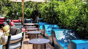 An outdoor seating area with multiple tables and chairs, surrounded by lush greenery and a pool. - Motel One Wien-Westbahnhof (Vienna)