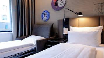 Ein Hotelzimmer mit zwei Einzelbetten, einem Nachttisch, einer Lampe und einer Wand mit Kunstwerken.