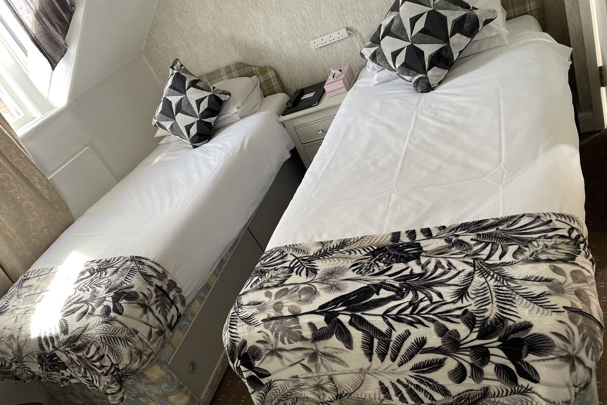 Un lit simple avec un coussin aux motifs géométriques et une couverture à motifs floraux.