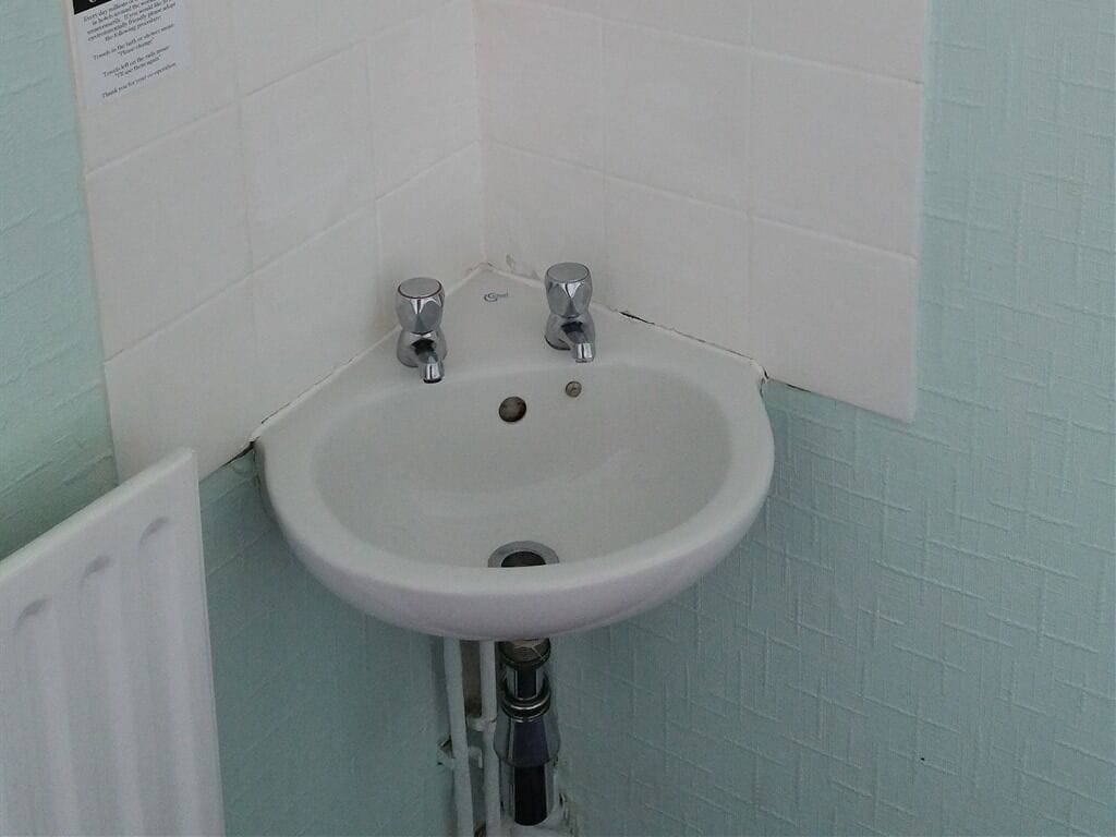Casa de banho com uma pia branca, duas torneiras e um radiador branco.