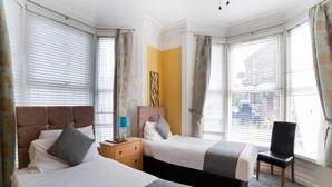 Ein Hotelzimmer mit zwei Betten, einem Sessel, einem Nachttisch und einem Bild an der Wand.
