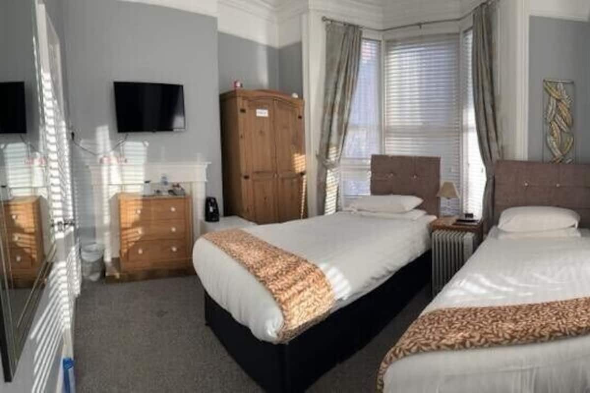 Une chambre d’hôtel avec deux lits, une armoire, un téléviseur à écran plat et de grandes fenêtres équipées de stores.