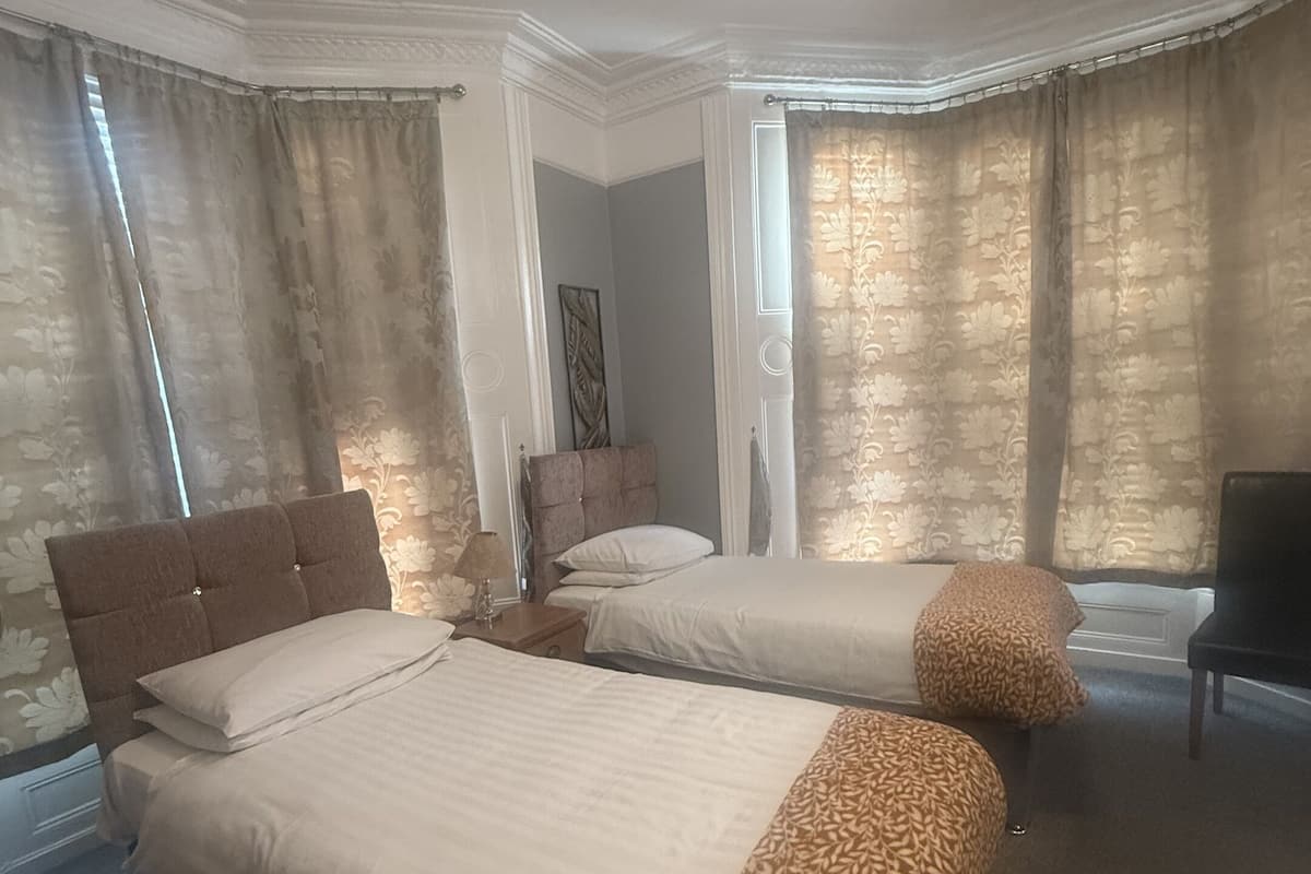 Une chambre d’hôtel avec deux lits, un canapé, un fauteuil et une grande fenêtre avec des rideaux.