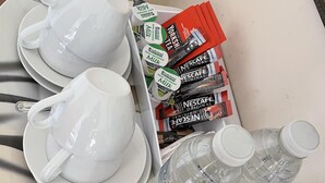 Ein Tablett mit weißen Tassen, Untertassen, Nescafe Original Packungen, Wasserflaschen und Lotus Keksen.