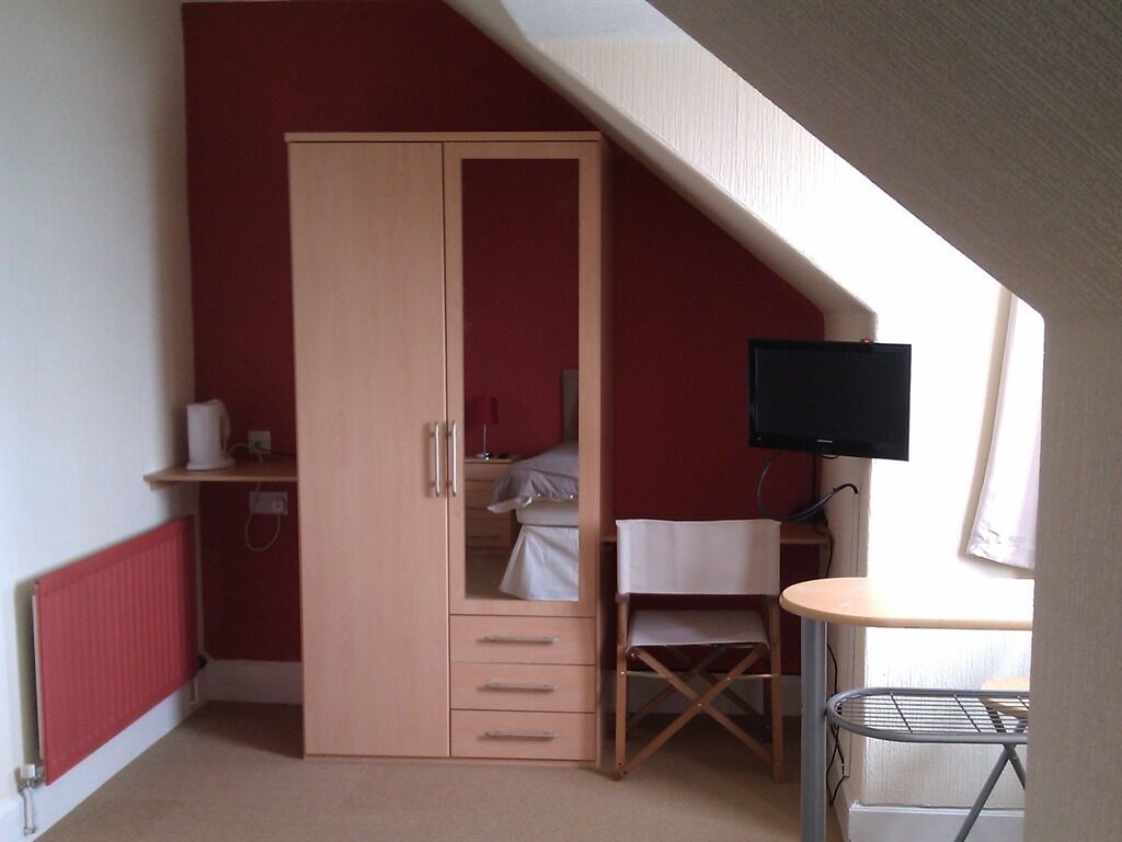 A bedroom with a wardrobe, a bed, a desk, and a television.