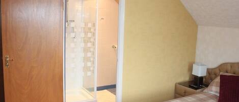 A bedroom with a bed, a nightstand, a lamp, and a door leading to a bathroom with a shower.