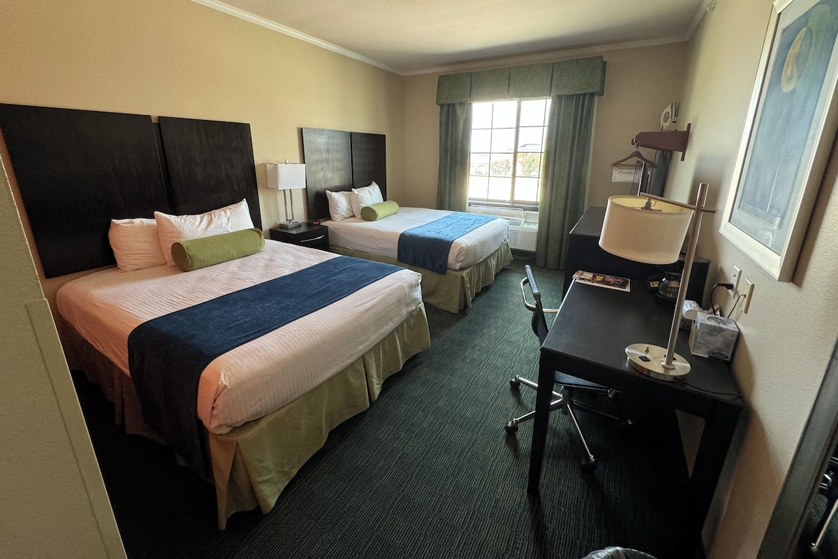Een hotelkamer met twee bedden, een bureau, een stoel, een lamp en een raam met gordijnen.