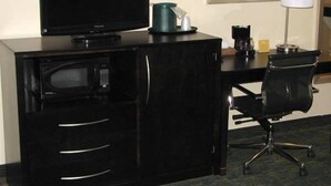 A hotel room with a black desk, a television, a coffee maker, and a chair. - Cityview Inn & Suites Downtown RiverCenter Area (San Antonio)