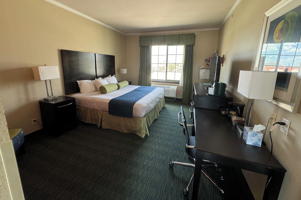Een hotelkamer met een bed, nachtkastjes, een bureau, een stoel, een televisie en een raam met gordijnen.