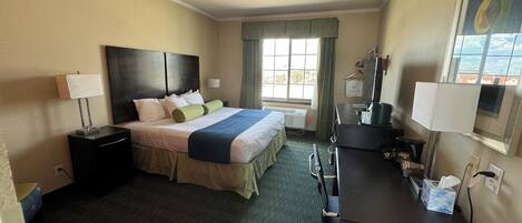 A hotel room with a bed, bedside tables, a desk, a chair, a TV, and a window with curtains.