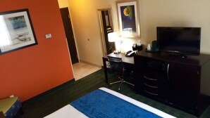 A hotel room with a bed, a desk with a chair, a television, and a painting on the wall. - Cityview Inn & Suites Downtown RiverCenter Area (San Antonio)