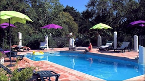 Piscina con sillas de descanso y sombrillas, rodeada de árboles.