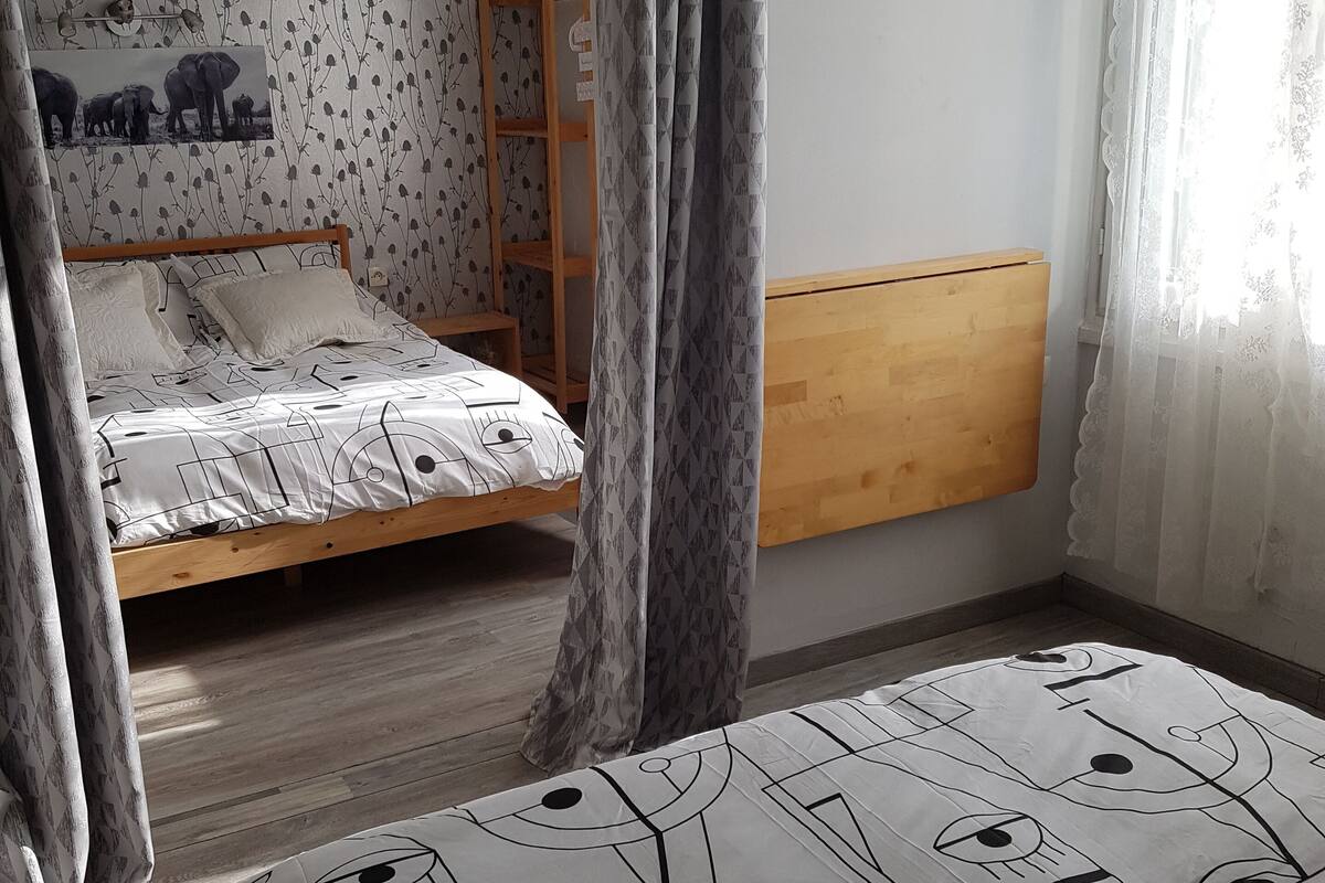A bedroom with a bed, a TV mounted on the wall, and a window with curtains.