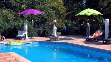 A swimming pool with lounge chairs and umbrellas, surrounded by greenery.