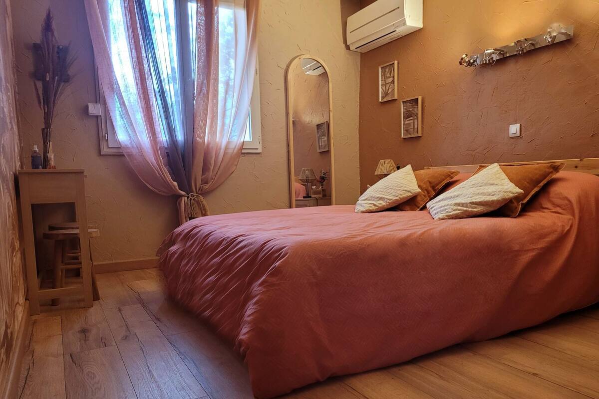 A bedroom with a large bed, wooden flooring, a mirror, and a window with curtains.