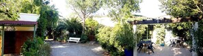 Un jardín con un sendero de grava, un banco de madera y una pérgola con sillas.